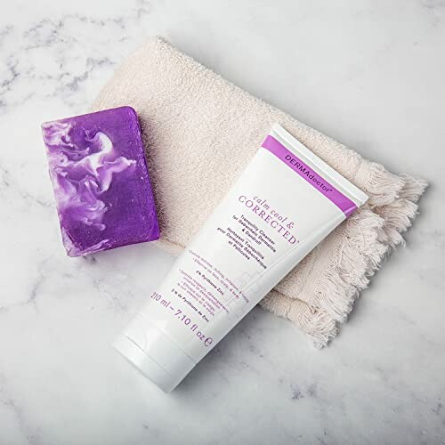 Skincare cream tube and purple soap on a beige towel