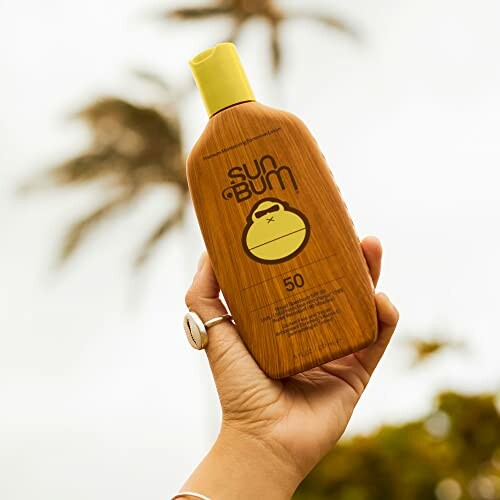 Hand holding Sun Bum sunscreen bottle with palm tree in background