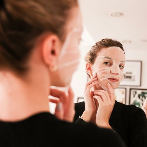 Woman applying a face mask in front of a mirror.