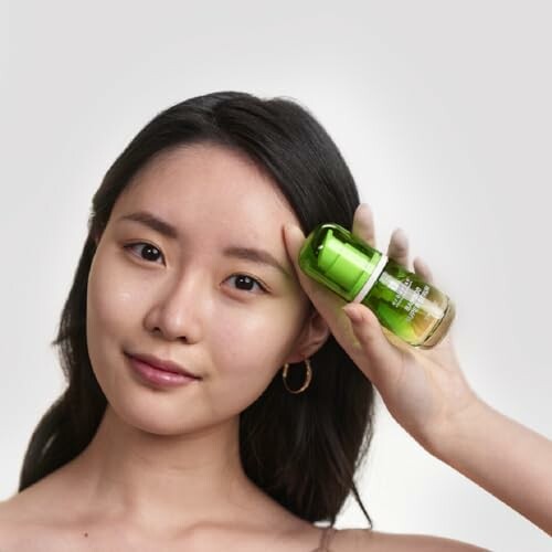 Woman holding a green skincare bottle near her face.