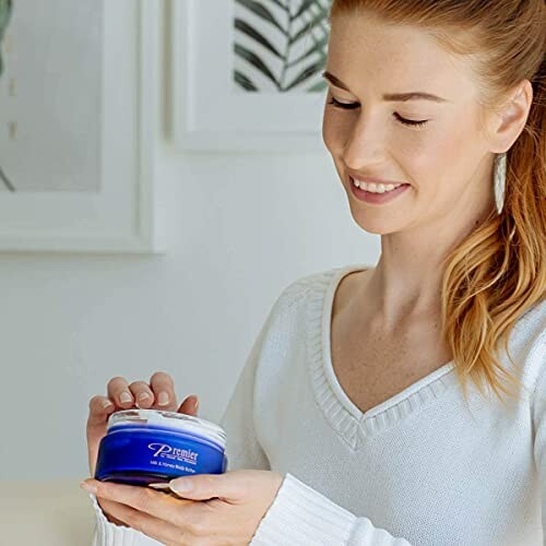 Woman holding a jar of blue skincare cream.