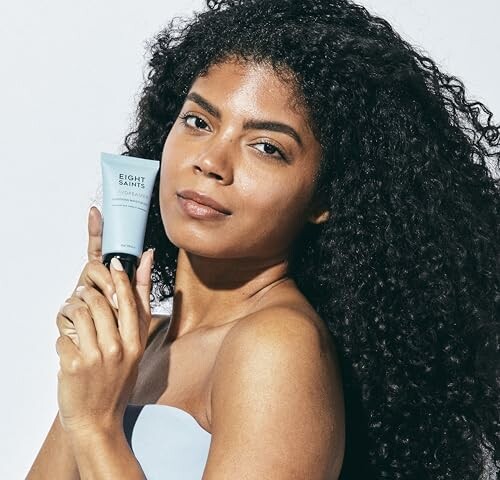 Woman with curly hair holding skincare product. 