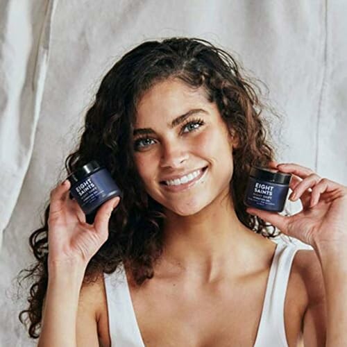 Woman smiling and holding two jars of skincare products.